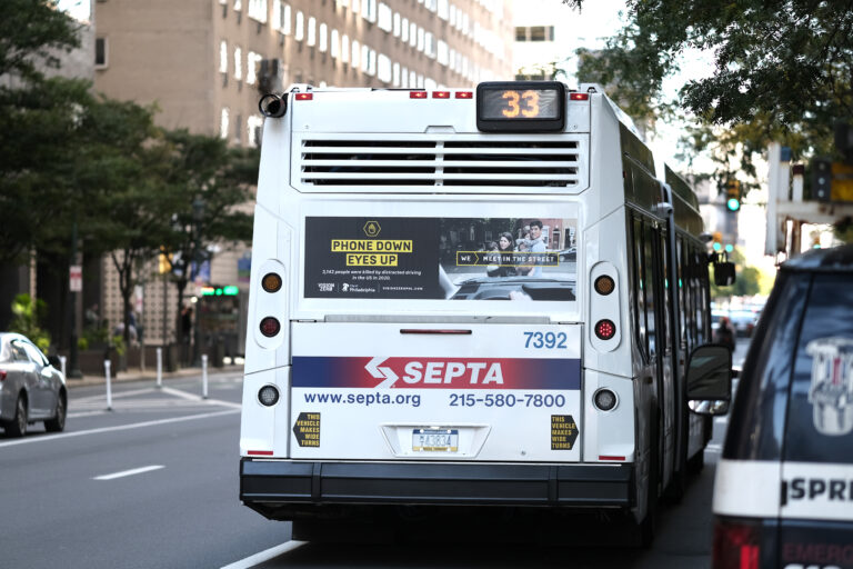 A bus driving down the street with an advertisement on the back that reads "Phone Down Eyes Up"